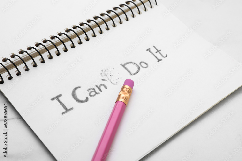 Motivation concept. Notebook with changed phrase from I Can't Do It into I Can Do It by erasing letter T on white table Motivation concept. Notebook with changed phrase from I Can't Do It into I Can Do It by erasing letter T on white table