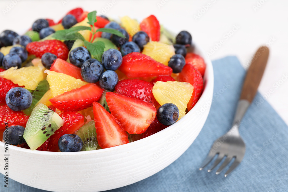 Delicious fresh fruit salad in bowl served on white table, closeup