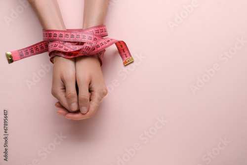 Woman tied with measuring tape on pink background, top view and space for text. Diet concept