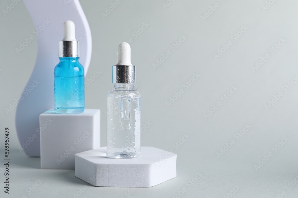 Presentation of bottles with cosmetic serums on light grey background, space for text Presentation of bottles with cosmetic serums on light grey background, space for text