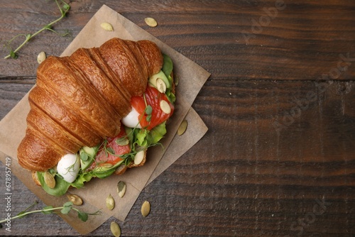 Tasty croissant with salmon, avocado, mozzarella and lettuce on wooden table, top view. Space for text