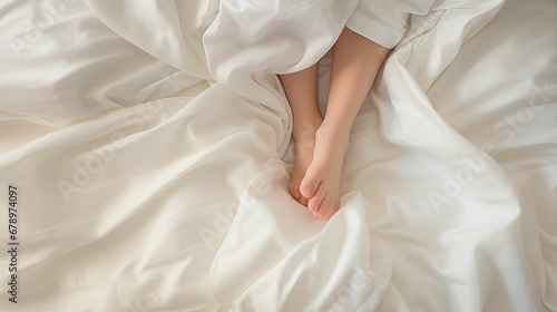 Close-up of a child's legs covered with soft white bed linen.