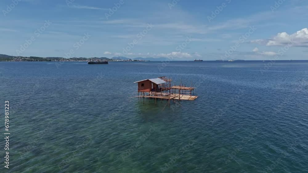 A wooden fisherman's hut on stilts in shallow waters with mountainous landscape in the distance. Balibayon, Surigao City - Philippines. Daytime, aerial drone shot. A wooden fisherman's hut on stilts in shallow waters with mountainous landscape in the distance. Balibayon, Surigao City - Philippines. Daytime, aerial drone shot.