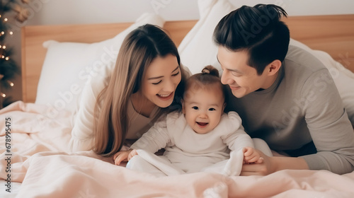 Happy asian family couple playing with cute baby child in bed. Cheerful mom, dad, and daughter relaxing and smiling on the bed
