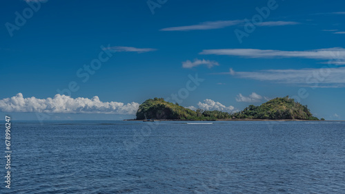 The beautiful tropical island is covered with green vegetation. Boats are visible near the shore. Ripples on the blue water. Clouds in the azure sky. copy space. Madagascar. Nosy Sakatia photo
