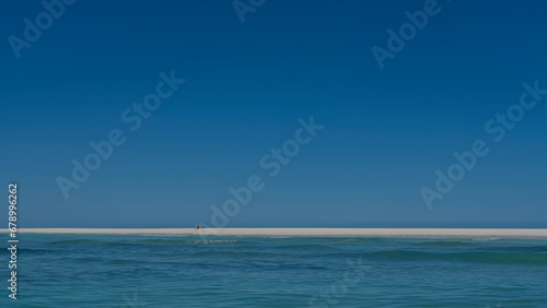 Marine minimalist idyll. Calm turquoise ocean. Clear azure sky. Tiny silhouettes of people can be seen on the sandy beach in the distance. Copy space. Madagascar. Nosy Iranja