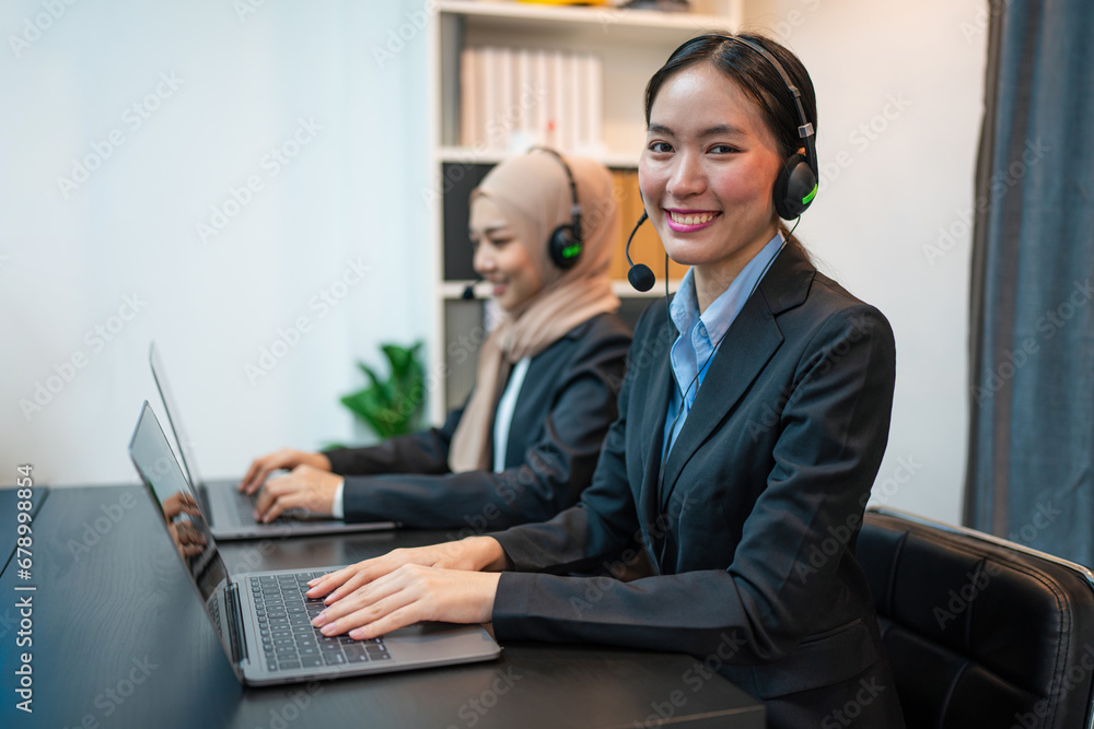 Friendly smiling woman call center operator with headset using computer, Customer service, Call center worker accompanied by her team at office. Friendly smiling woman call center operator with headset using computer, Customer service, Call center worker accompanied by her team at office.