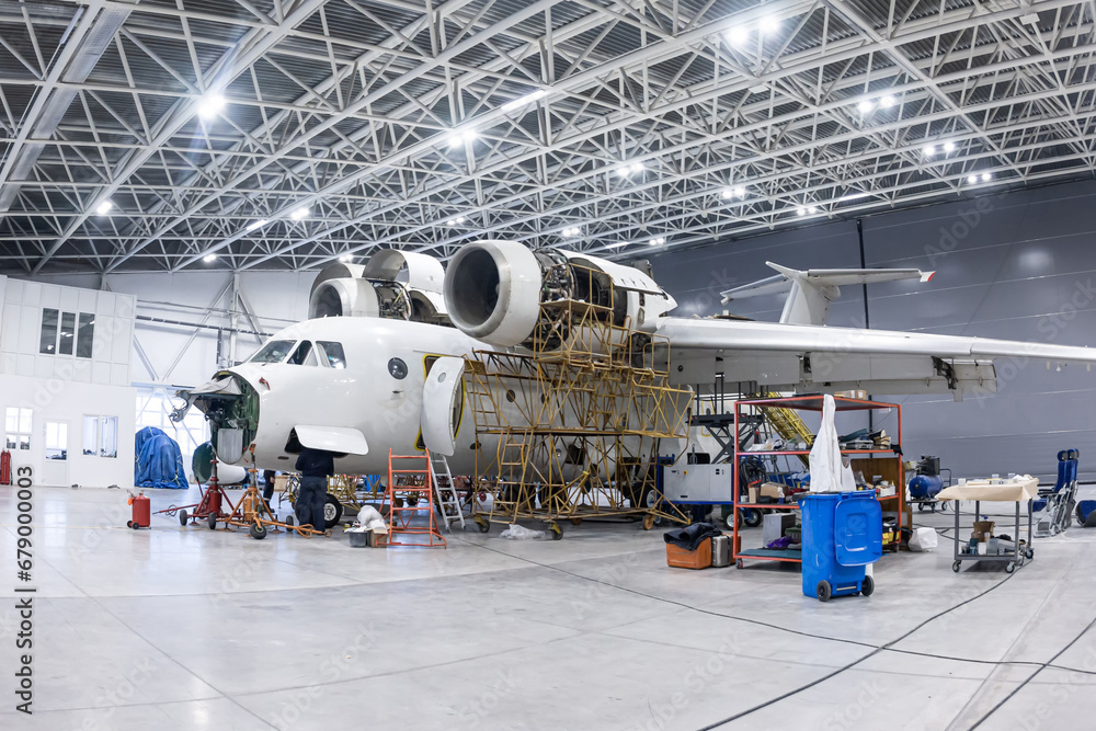 White transport aircraft in the aviation hangar. Airplane under maintenance. Checking mechanical systems for flight operations - obrazy, fototapety, plakaty 