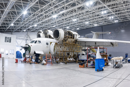 White transport aircraft in the aviation hangar. Airplane under maintenance. Checking mechanical systems for flight operations photo