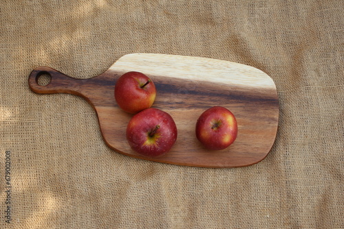 Three red apples on a wooden cutting board