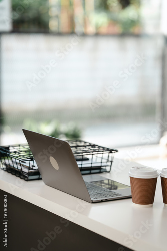 silver laptop on a desk with a blurred background. Nearby are two takeaway coffee cups and a wire basket.