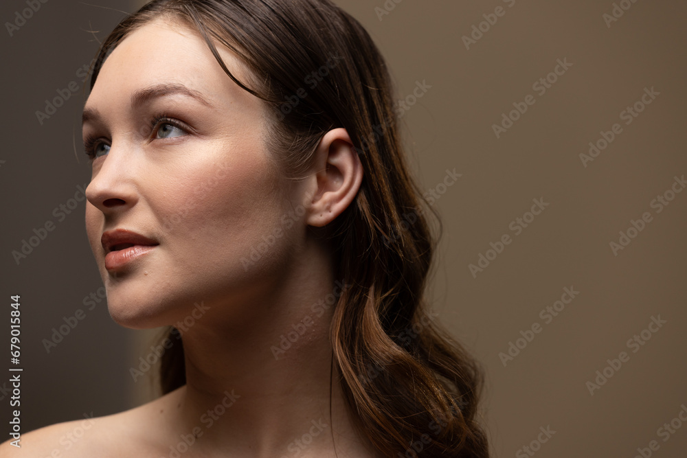 Fototapeta premium Caucasian woman with brown hair wearing natural makeup on beige background, copy space