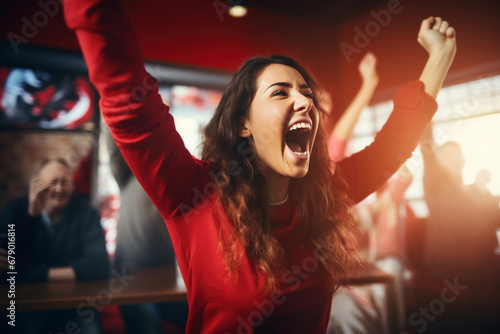 A female sports fan is happy with a group of friends, many cheering together happily and excited to watch their favorite football team. Cheering sports fans wear red and white cheer team shirts.