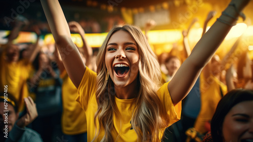 A female sports fan is happy with a group of friends, many cheering together happily and excited to watch their favorite football team. Cheering sports fans wear yellow cheer team shirts.
