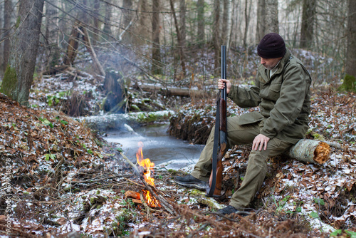 a hunter is sitting by a campfire in a remote forest