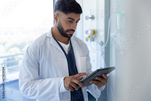 Biracial male doctor using tablet in sunny hospital room photo