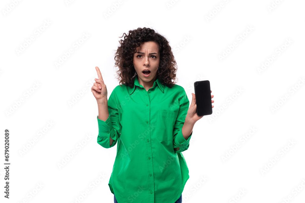 young employee of the company woman with black hair dressed in a green shirt shows the smartphone screen in surprise young employee of the company woman with black hair dressed in a green shirt shows the smartphone screen in surprise