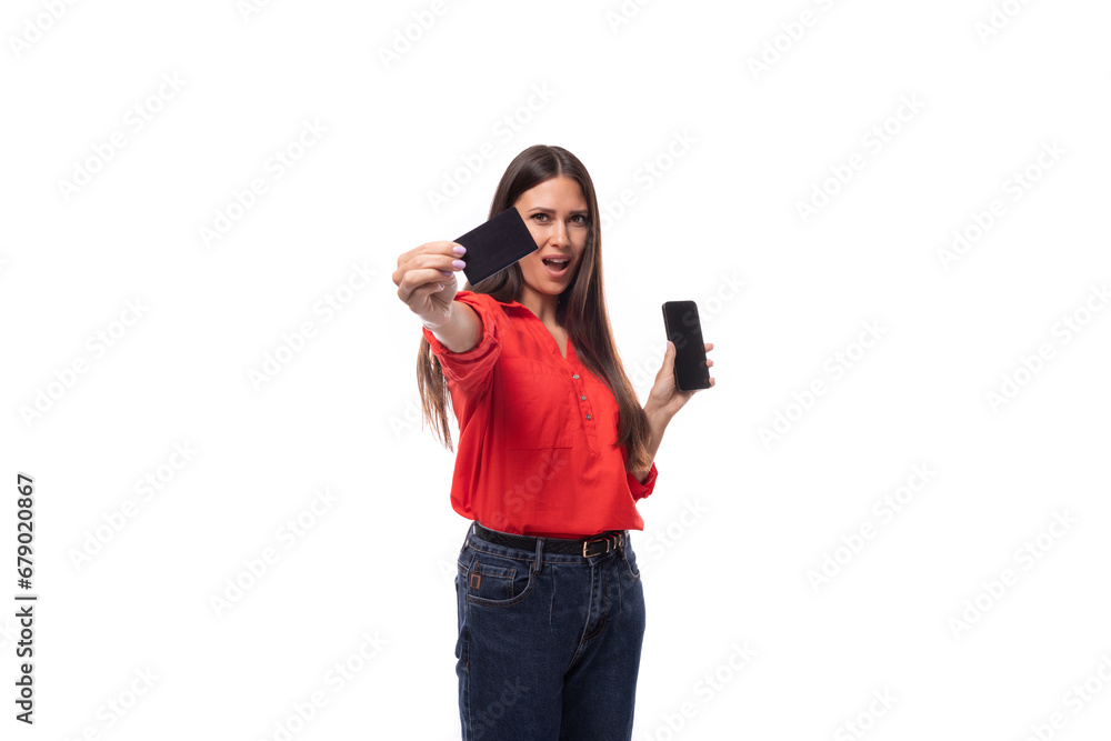 Fototapeta premium pretty confident successful young brunette business woman dressed in red blouse showing credit card and smart phone on white background with copy space