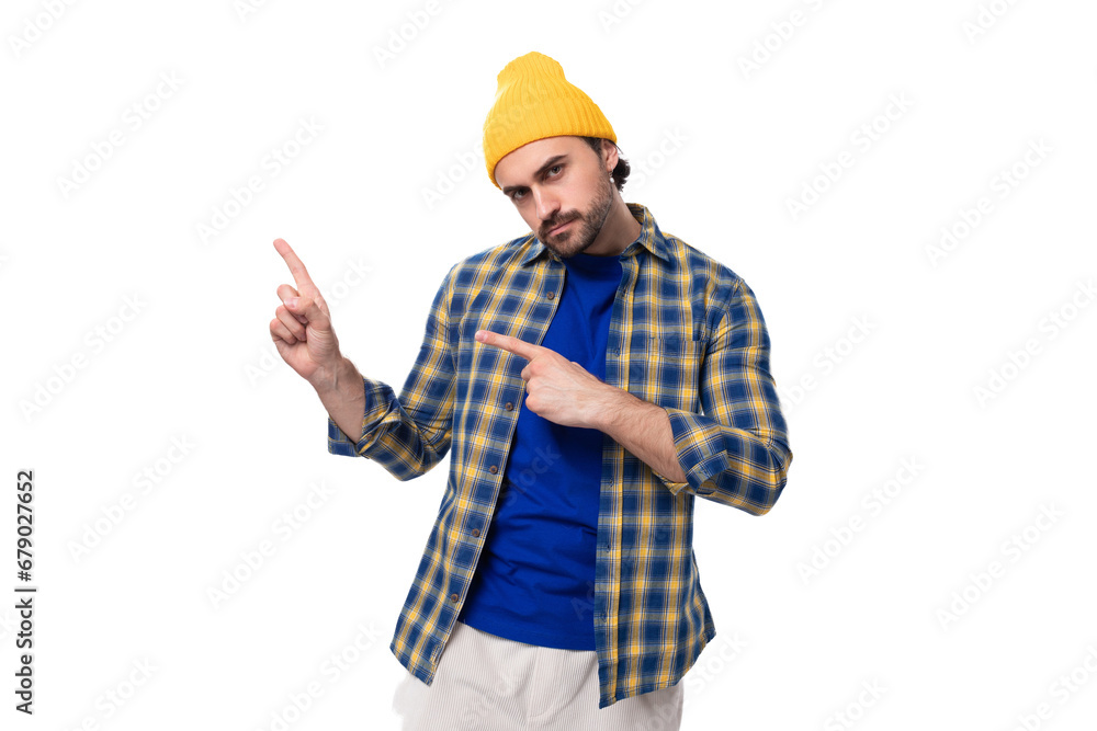 handsome young hipster man in a cap and shirt points his hand to the side on a white background with copy space