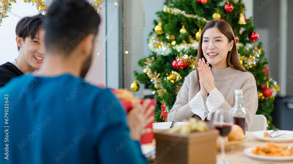 Asian cheerful happy female in warm sweater receiving wrapped present gift box from unrecognizable male friend in blurred foreground celebrating Christmas eve and New Year with decorative Xmas tree Asian cheerful happy female in warm sweater receiving wrapped present gift box from unrecognizable male friend in blurred foreground celebrating Christmas eve and New Year with decorative Xmas tree