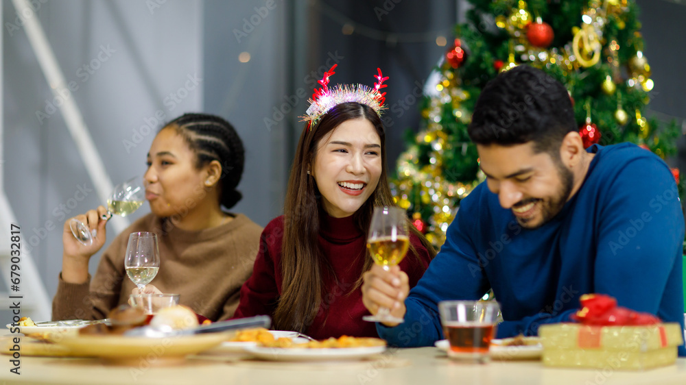 Group of Asian Indian happy cheerful male female friends wears reindeer antlers headband cheers toasting champagne beverage glasses together on dinner table celebrating Christmas eve in dining room Group of Asian Indian happy cheerful male female friends wears reindeer antlers headband cheers toasting champagne beverage glasses together on dinner table celebrating Christmas eve in dining room