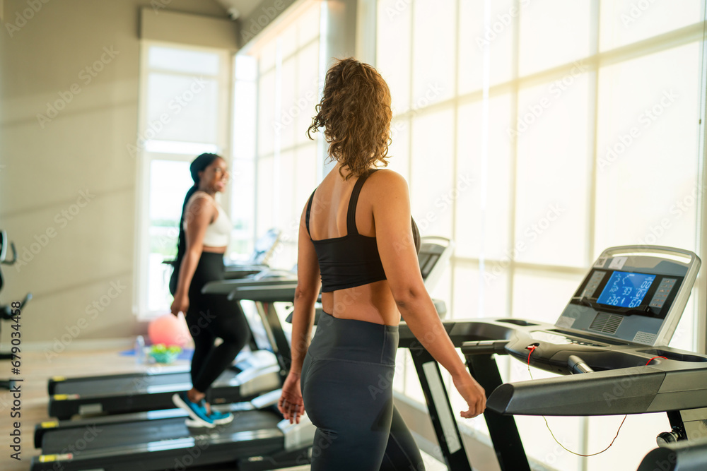 Fitness exercising in gym. Sporty woman in a sports bra doing exercise by running on treadmill during a workout at the gym fitness center with group of people. Fitness exercising in gym. Sporty woman in a sports bra doing exercise by running on treadmill during a workout at the gym fitness center with group of people.
