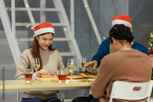 Group of Asian Indian happy cheerful male female friends wears reindeer antlers headband eating food with champagne beverage glasses together on dinner table celebrating Christmas eve in dining room