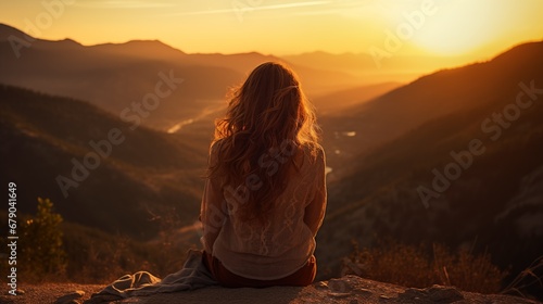 a woman sitting on top of a mountain at sunset © Nick
