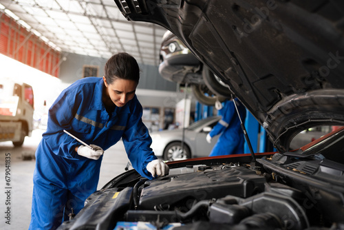 Mechanic working under the hood at the repair garage. Portrait of a happy mechanic woman working on a car in an auto repair shop. Female mechanic working on car. Female Auto Mechanic.