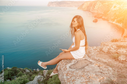 Happy woman in white shorts and T-shirt, with long hair, talking on the phone while enjoying the scenic view of the sea in the background. © svetograph
