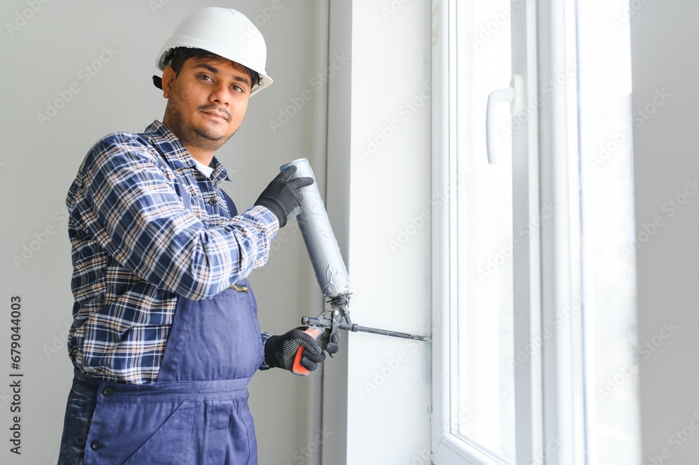 Indian worker using a silicone tube for repairing of window indoor