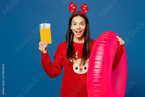 Traveler Latin woman in red Christmas sweater hold rubber ring passport ticket isolated on plain blue background Tourist travel abroad in free time rest getaway Air flight trip Happy New Year concept #679063839