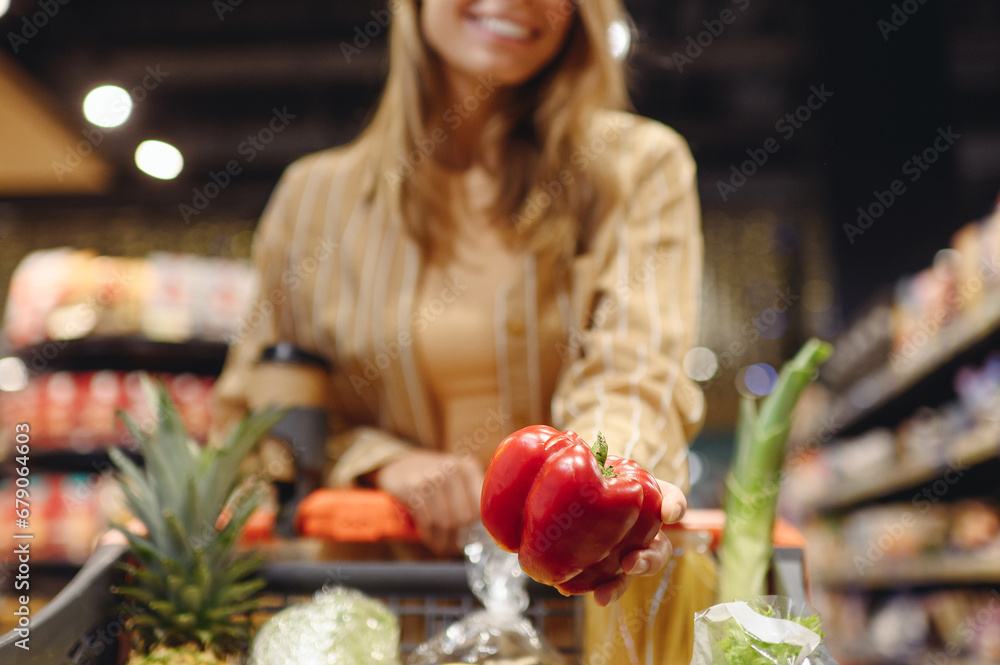 Cropped young customer woman wear casual clothes hold bell pepper shopping at supermaket store grocery shop buy with trolley cart choose products inside hypermarket Purchasing food gastronomy concept