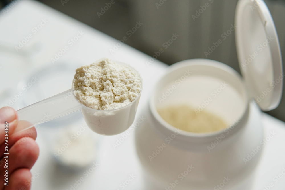 Young man with measuring spoon puts portion of whey protein powder into a shaker on wooden table, making protein drink. Young man with measuring spoon puts portion of whey protein powder into a shaker on wooden table, making protein drink.
