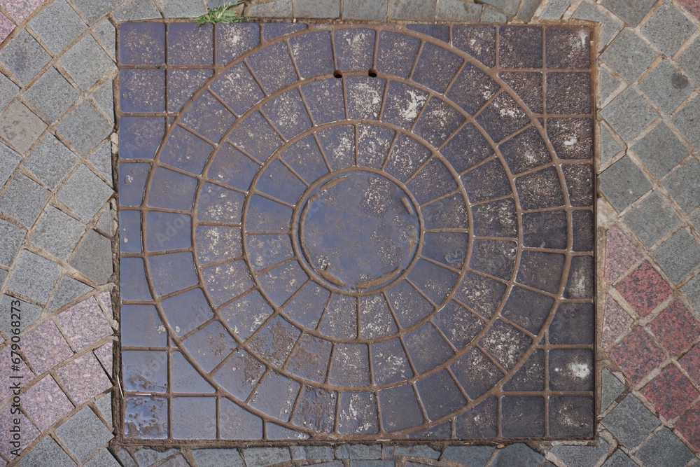 Rusty circular iron manhole cover on the sidewalk. Circular metal plate covering road water drainage
