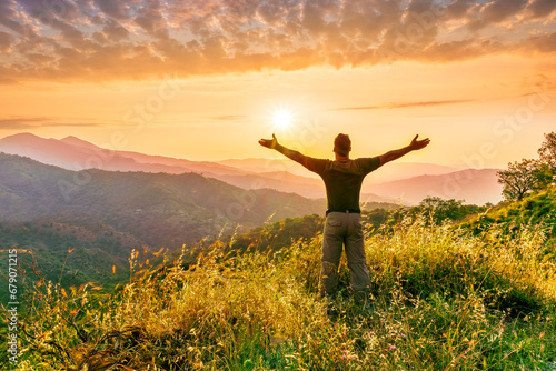 rejoicing man with beautiful scenic mountain sunset landscape on background. happy man watching amazing evening sunset