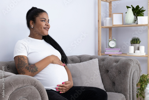 Pregnant African American woman in room on couch.