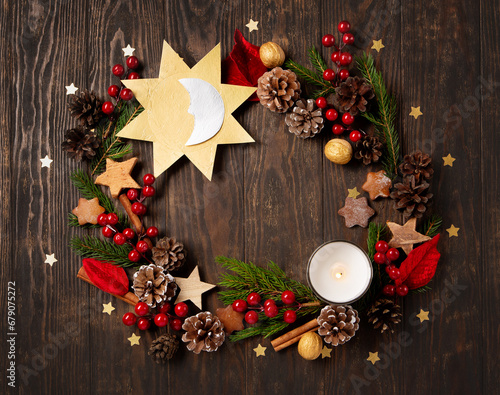 Winter solstice day, December 21. Sun and moon symbol, Christmas trees, pine cones, paddub branches with red berries, candle on dark wooden background, top view. photo