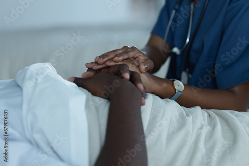 African american female doctors and male patient is lying in bed holding hands in hospital room photo