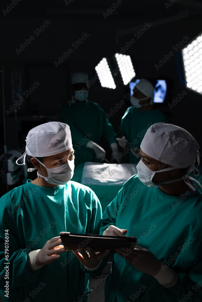 Diverse female surgeons discussing work using tablet in operating theatre at hospital
