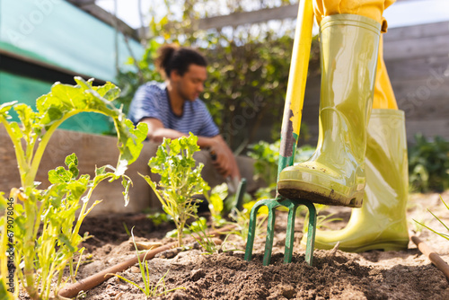 Legs of blonde caucasian woman loosening soil with fork in sunny greenhouse photo