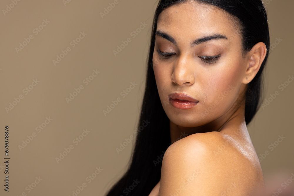 Portrait of biracial woman with dark hair and natural make up looking down on brown background Portrait of biracial woman with dark hair and natural make up looking down on brown background