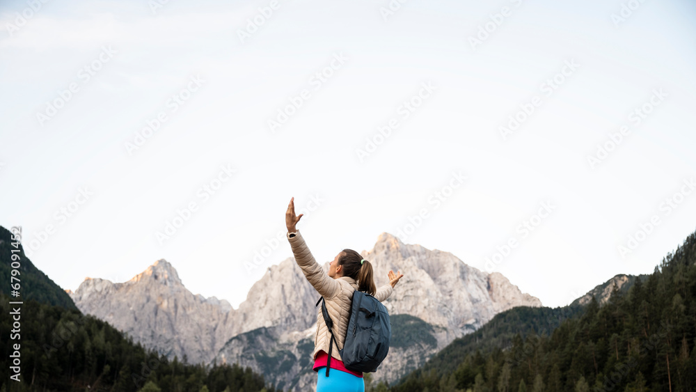 Happy young female hiker standing surrounded by beautiful high mountains with her arms spread wide