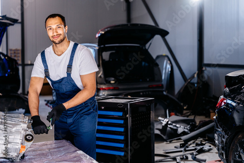 Car service, repair, maintenance and people concept. African american car mechanic with screwdriver repairing car engine of electric car automobile in workshop. © Iryna