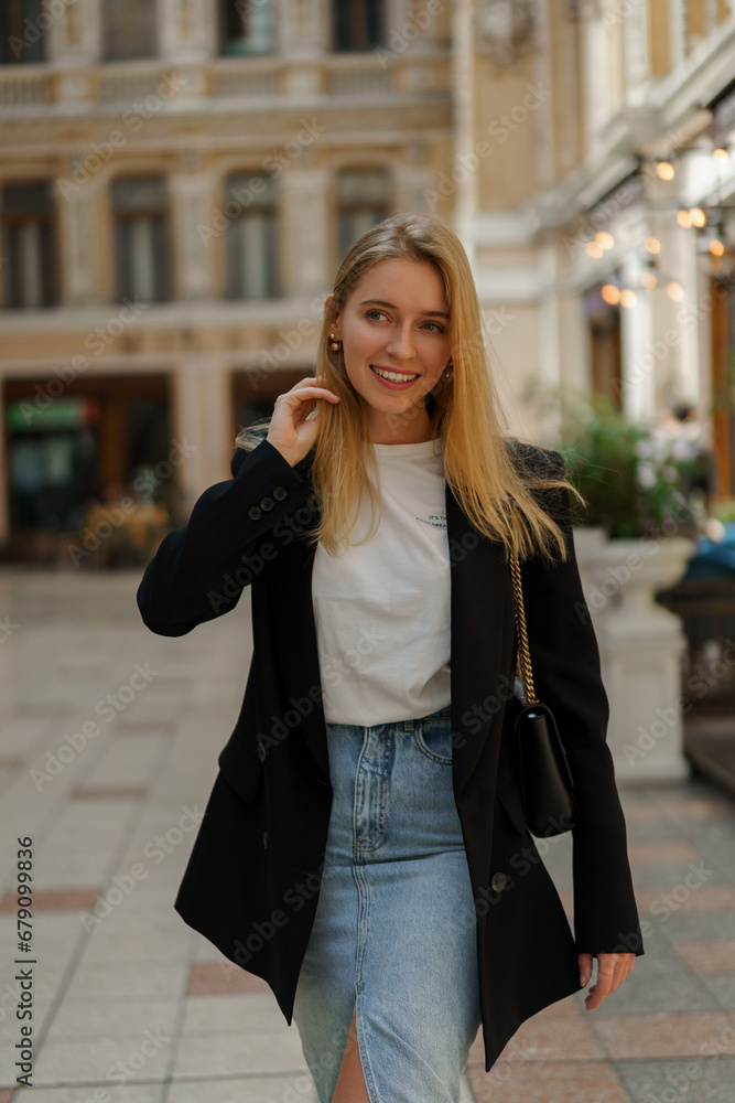 Fototapeta premium Pretty blond woman in stylish casual business outfit walking in beautiful european city.