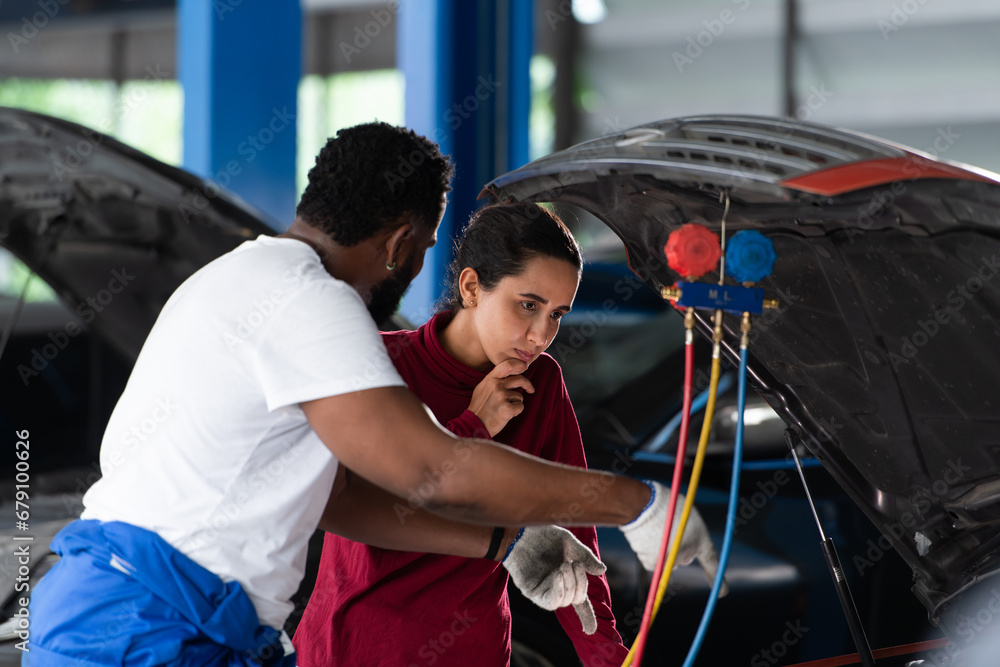 Car mechanic working in an auto repair shop explain to customer after inspecting the operation of the car's air conditioner and refrigerant