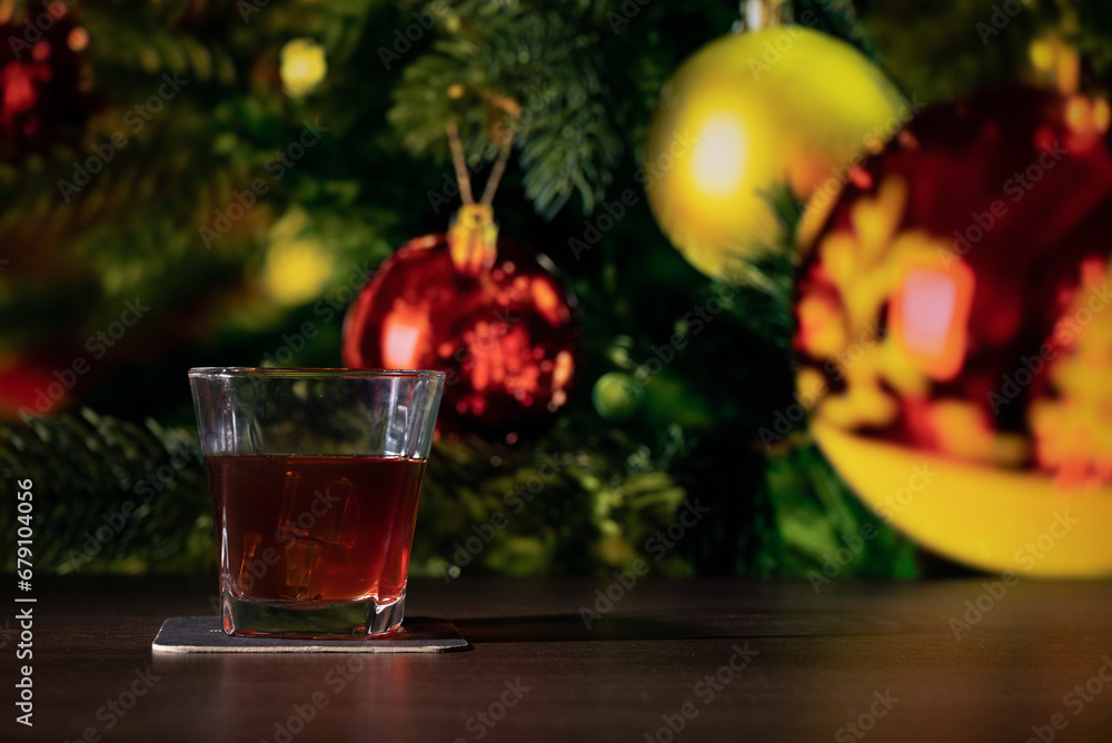 Glass of whiskey on the bar in front of the blur image Christmas home room with tree and festive bokeh lighting, blurred holiday background