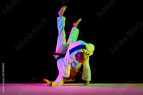 Portrait of sportsmen, martial arts fighters in white kimono fighting performing techniques in motions isolated black background. photo