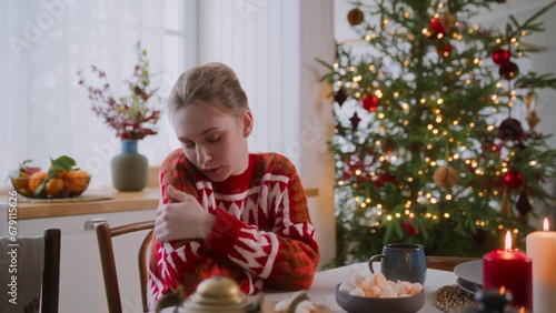 alone young woman sits at empty table in cozy home with Christmas tree, feels abandoned and heartbreak. Misses family, unhappy to loneliness in festive holiday
