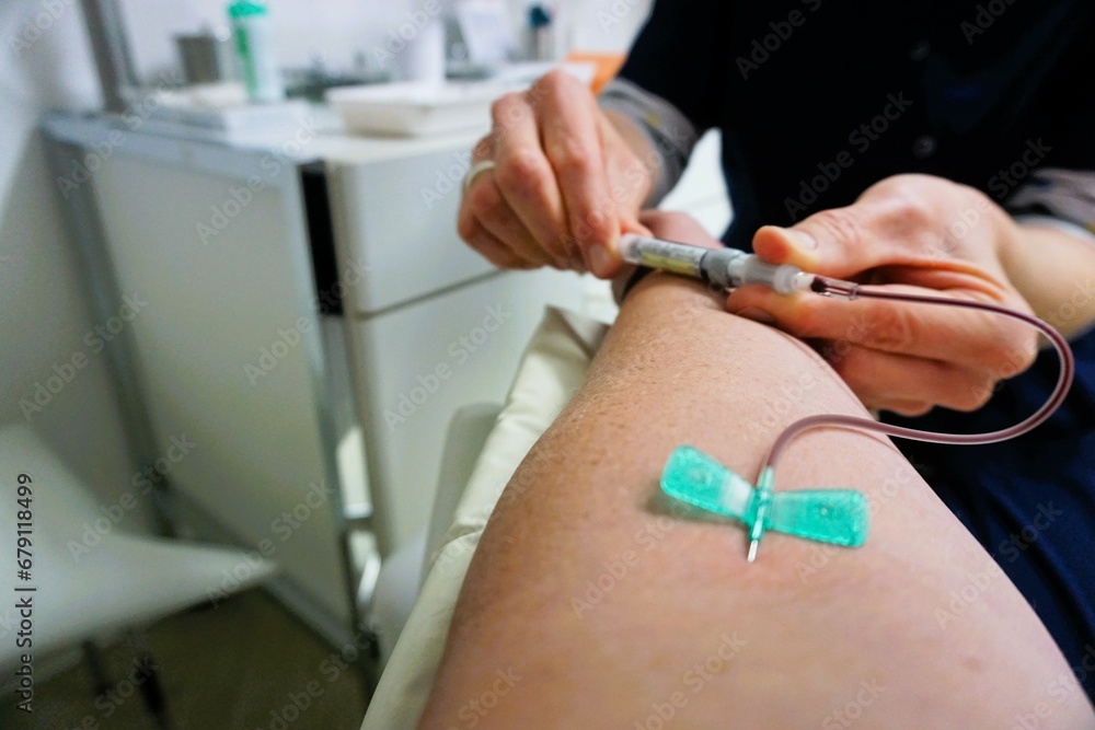 Abgestützter ausgestreckter Arm von Patientin bei Blutabnahme von Ärztin mit Röhrchen in Händen